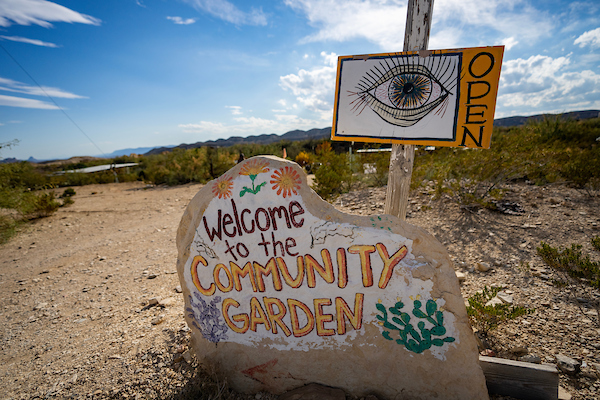 A large rock painted to look like a sign that says "Welcome to the Community Garden"