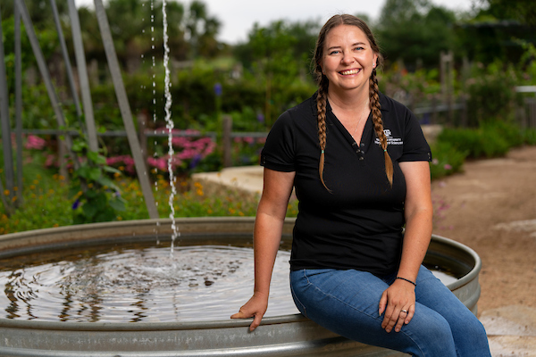 A woman in a black polo and jeans sits on the edge of a small pool