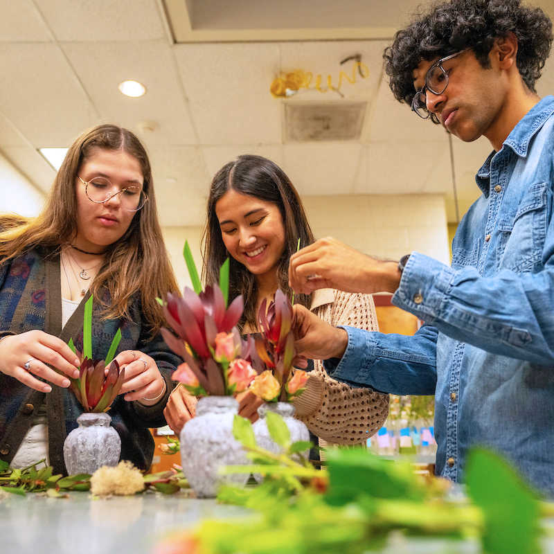 Three students work together arranging flowers in vases.
