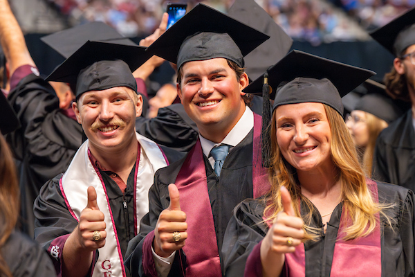 Group of students at graduation with their thumbs up (Gig 'Em)